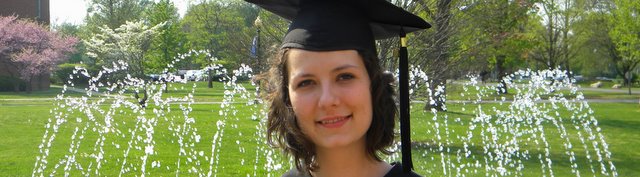 Photo of a student at graduation in front of a fountain.